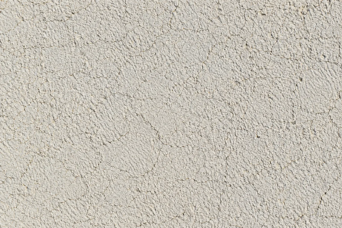 Réseau de fines craquelures sur un enduit de façade blanc cassé, révélé par une lumière rasante